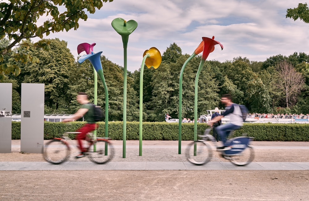 a couple of people riding bikes past a sculpture