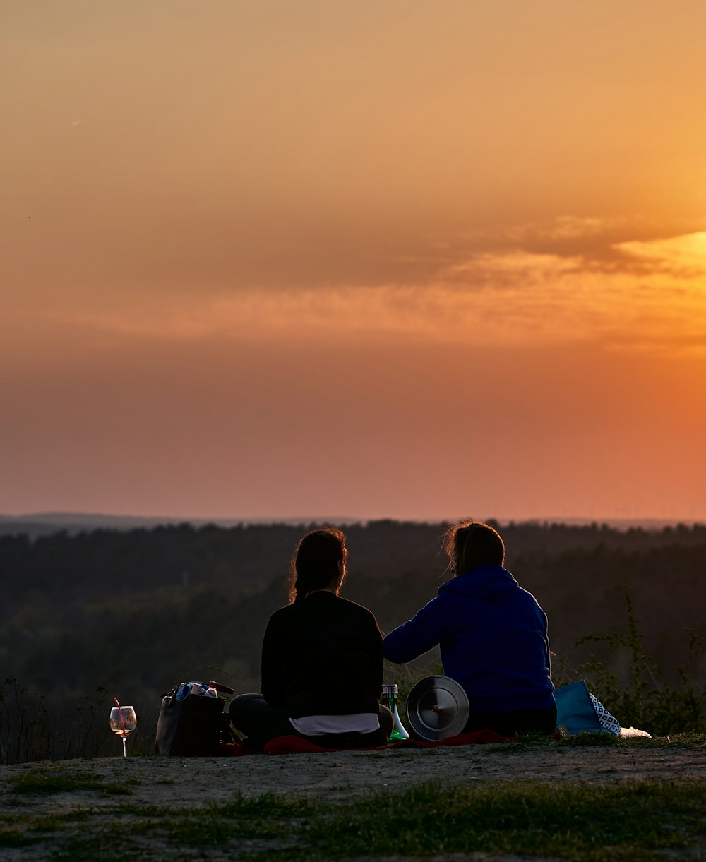two people sitting on a hill watching the sun set