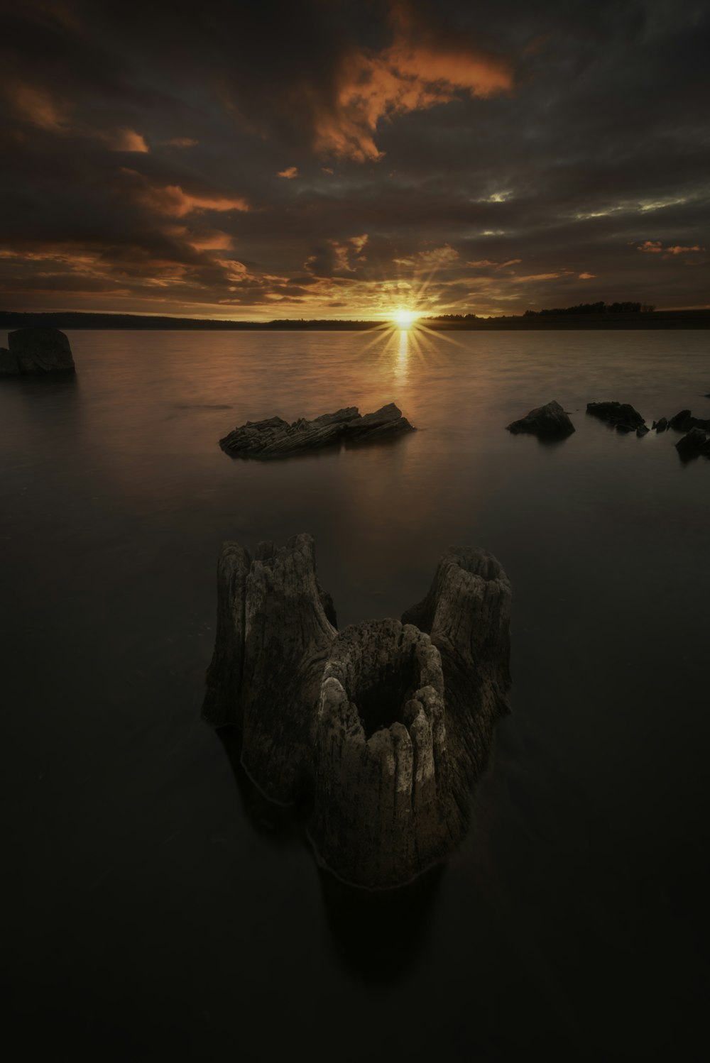 a sunset over a body of water with rocks in the foreground