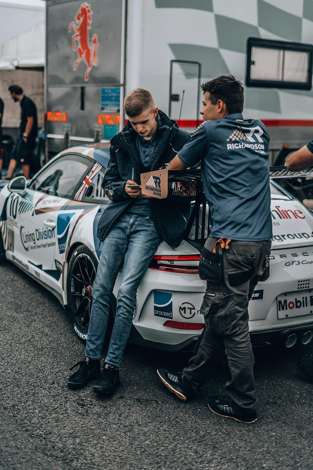 a man sitting on the back of a car next to another man