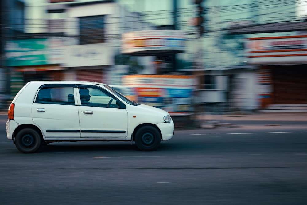 a small white car driving down a street