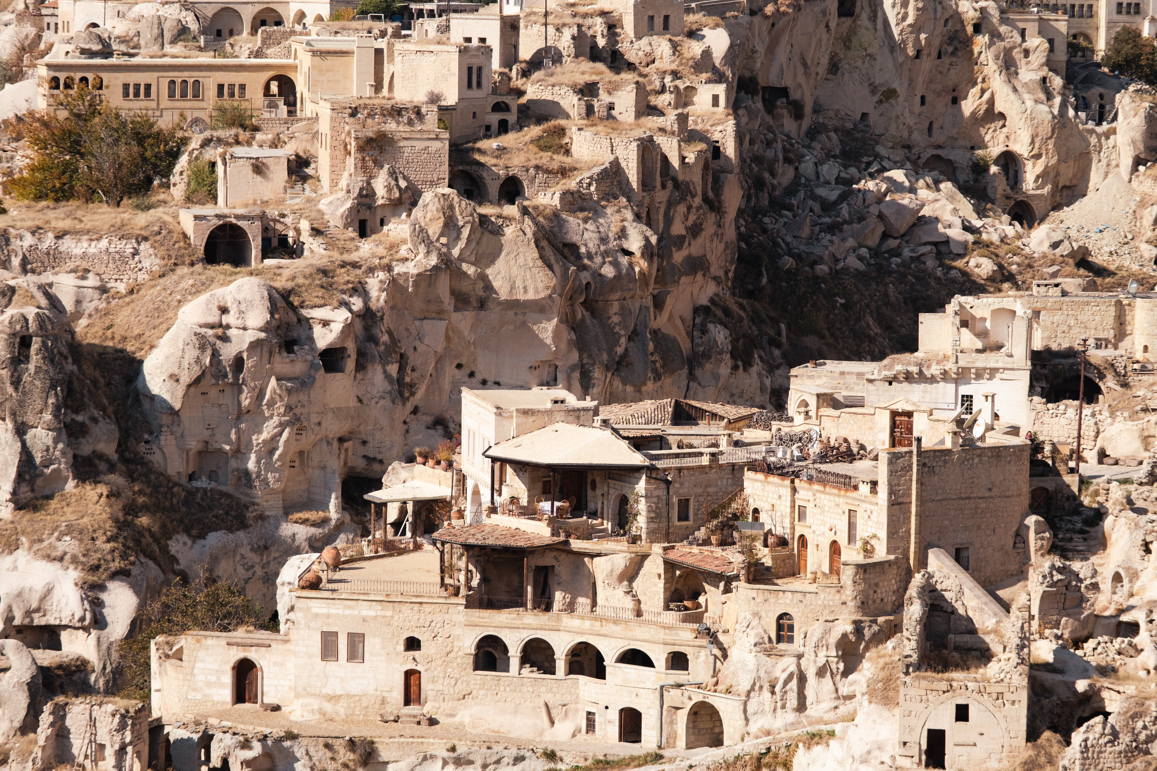 The old cave village of Ortahisar in Cappadocia, honey-coloured stone houses and rock-cut dwellings stacked in tiers up the soft tuff cliffs in low warm light
