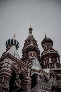 The image features a prominent architectural structure with ornate, onion-shaped domes. The domes have intricate designs, featuring a mix of colors such as green, white, and red. The structure showcases beautifully detailed arches and geometric patterns along the facade.