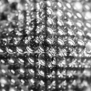 A collection of small transparent glass balls closely packed together, reflecting light in a symmetrical pattern that creates a textured and intricate appearance.