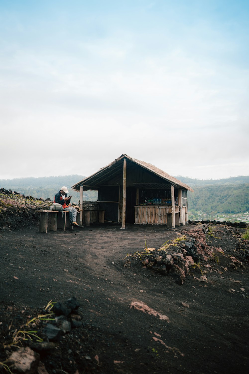 a man sitting on a bench in front of a hut