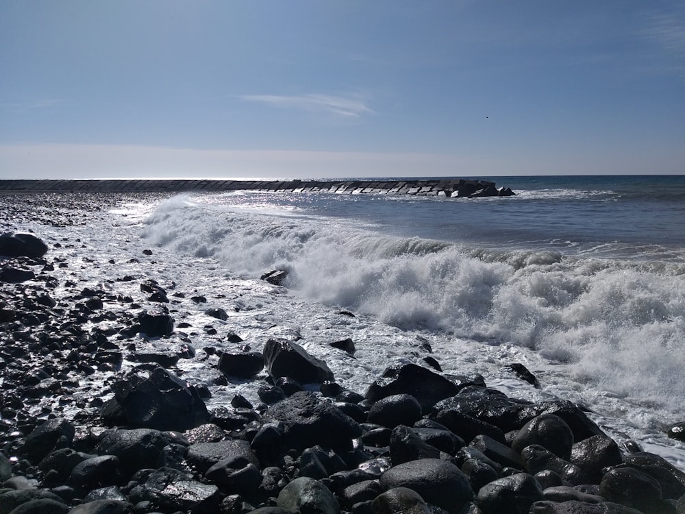 Una playa rocosa con una ola que llega a la orilla