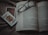 An open book lies on a textured fabric surface, with reading glasses placed on top. Beside the book, two playing cards, one featuring a jack of spades, are positioned off to the side.
