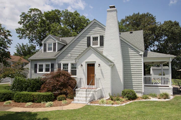 a gray house with a white porch and a brown door