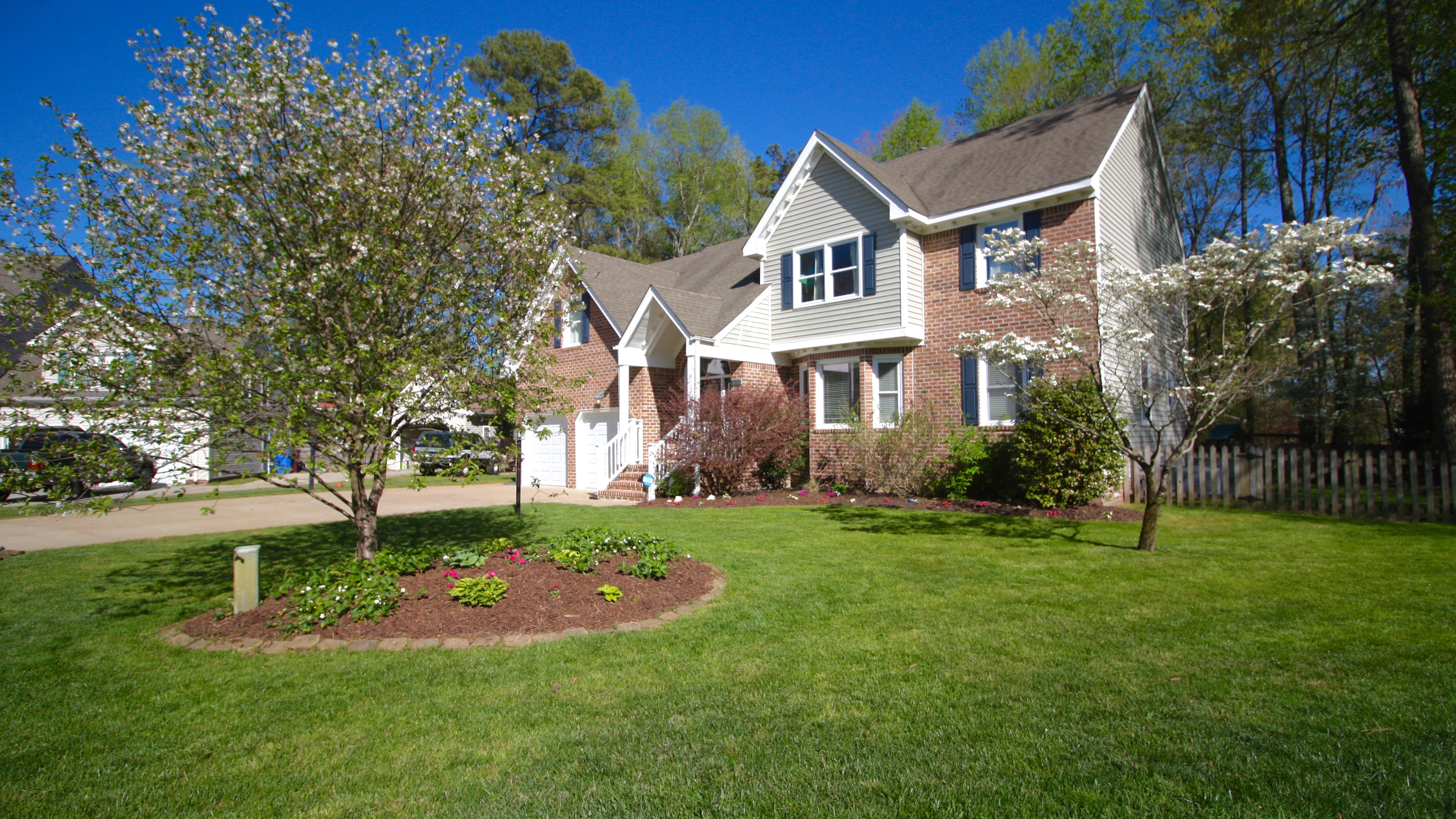 Brick and siding home with a flowering tree in a green front yard