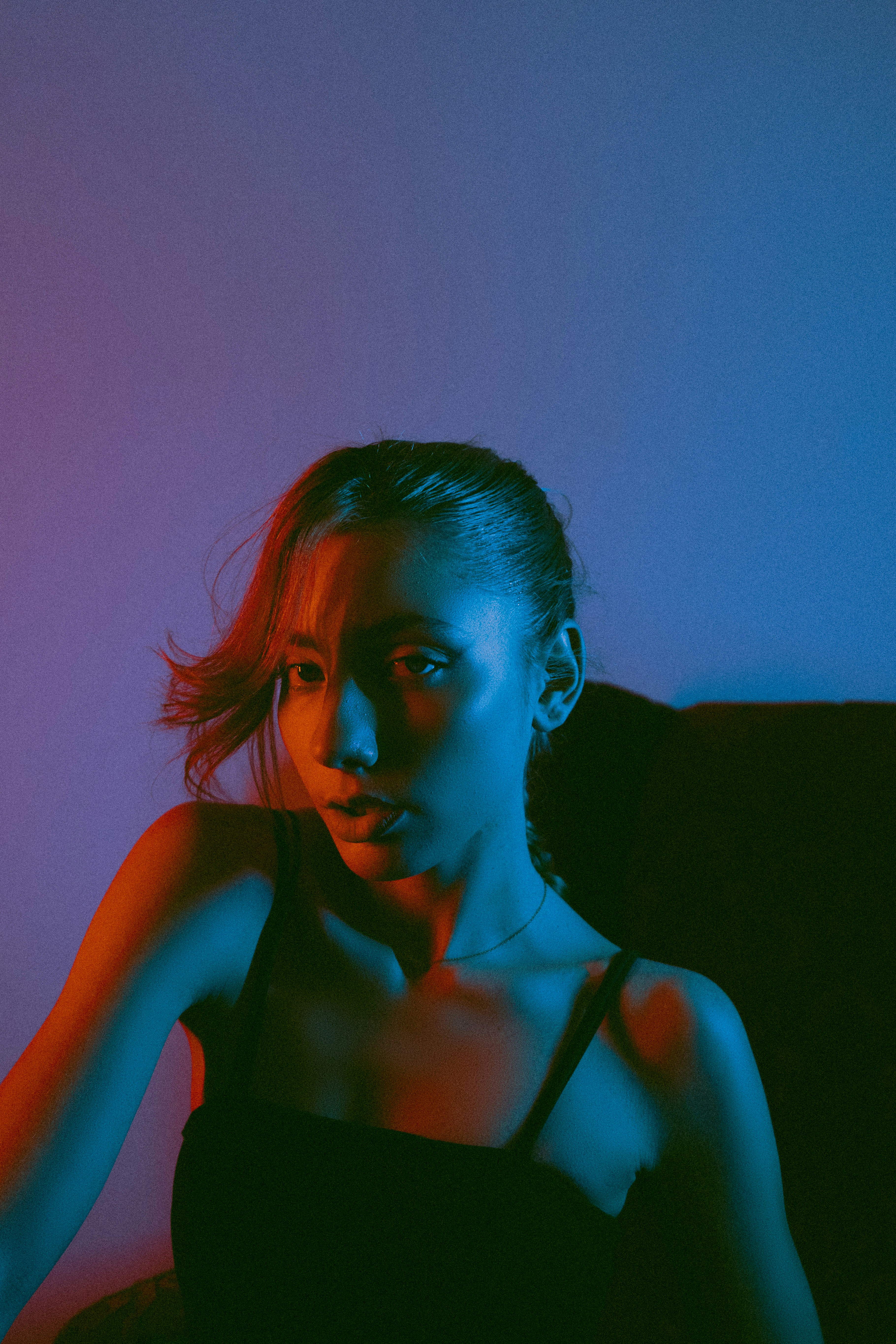 A woman sitting on a couch in a dark room photo – Free Blue Image on ...