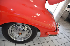 Before and after close-up of a classic car restored with deep red automobile paint, gleaming under bright workshop lights.