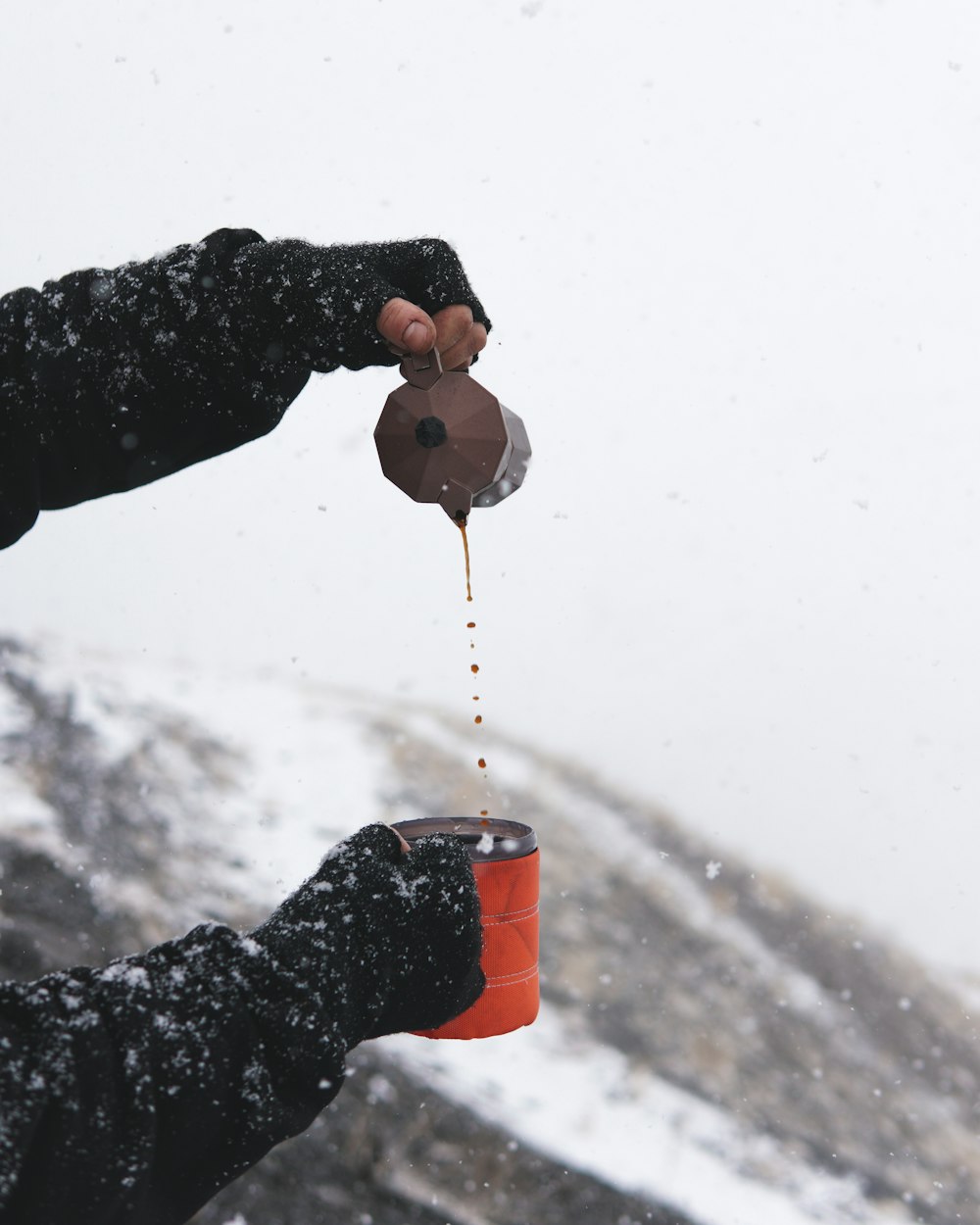 Eine Person, die Kaffee in eine Tasse im Schnee gießt