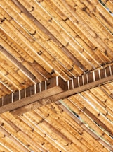 A close-up view of bamboo sticks arranged in a diagonal pattern, supported by wooden beams. The texture and natural grain of the bamboo and wood are clearly visible, showcasing earthy tones and a rustic feel.