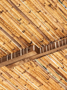 A close-up view of bamboo sticks arranged in a diagonal pattern, supported by wooden beams. The texture and natural grain of the bamboo and wood are clearly visible, showcasing earthy tones and a rustic feel.