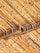 A close-up view of bamboo sticks arranged in a diagonal pattern, supported by wooden beams. The texture and natural grain of the bamboo and wood are clearly visible, showcasing earthy tones and a rustic feel.