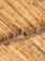 A close-up view of bamboo sticks arranged in a diagonal pattern, supported by wooden beams. The texture and natural grain of the bamboo and wood are clearly visible, showcasing earthy tones and a rustic feel.