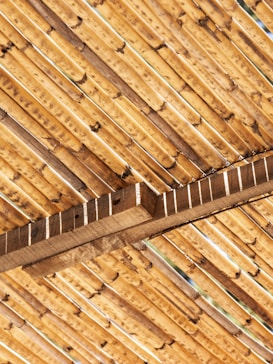 A close-up view of bamboo sticks arranged in a diagonal pattern, supported by wooden beams. The texture and natural grain of the bamboo and wood are clearly visible, showcasing earthy tones and a rustic feel.