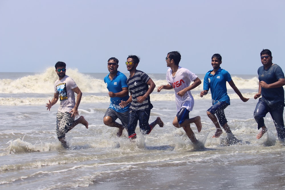 a group of men run through the water at the beach