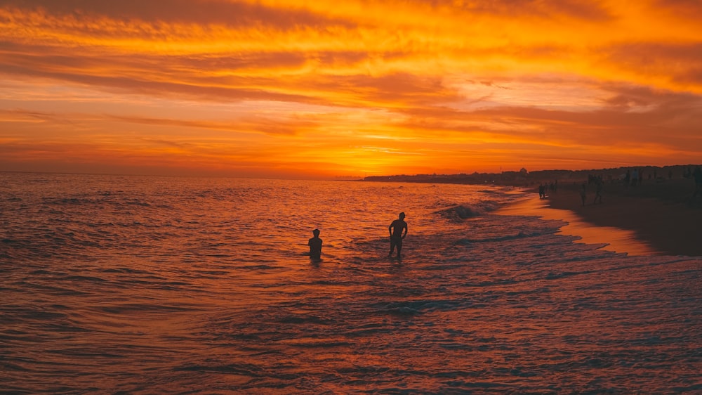 a couple of people standing on top of a beach next to the ocean