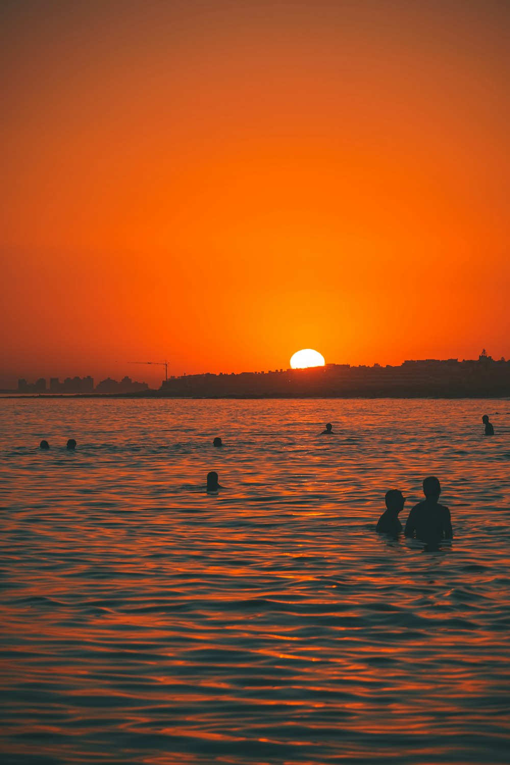 a group of people swimming in the ocean at sunset