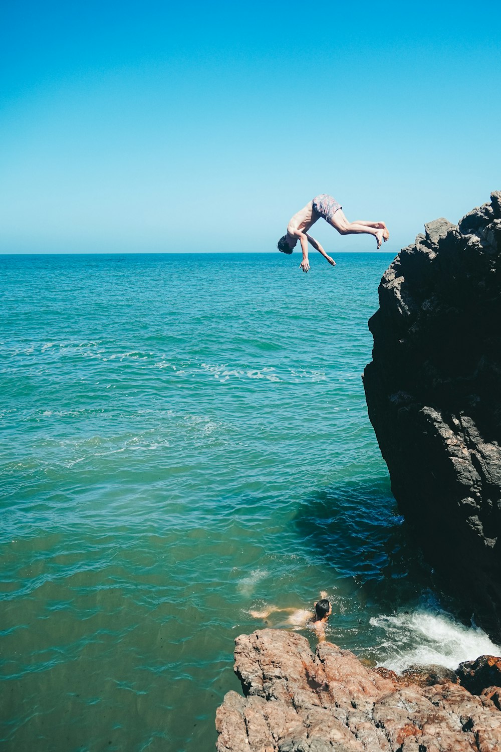 a person jumping off a cliff into the ocean