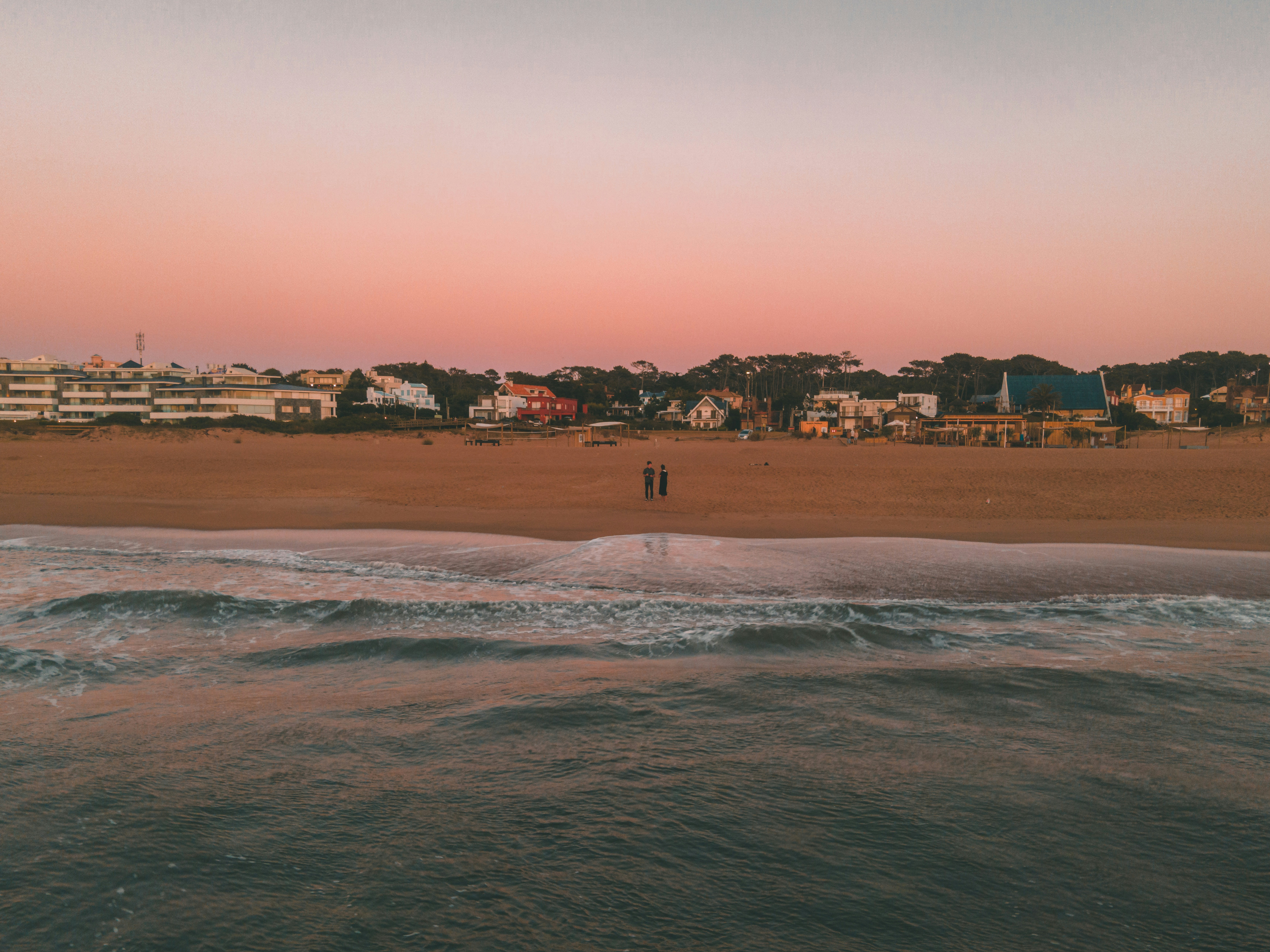 a couple of people standing on top of a sandy beach