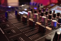 Close-up view of a professional DJ mixer with various knobs and sliders. The image captures the intricate details of the equipment, highlighting the texture of the knobs and the smooth surface of the sliders. Soft lighting adds a warm ambiance, casting gentle reflections on the mixer surface.