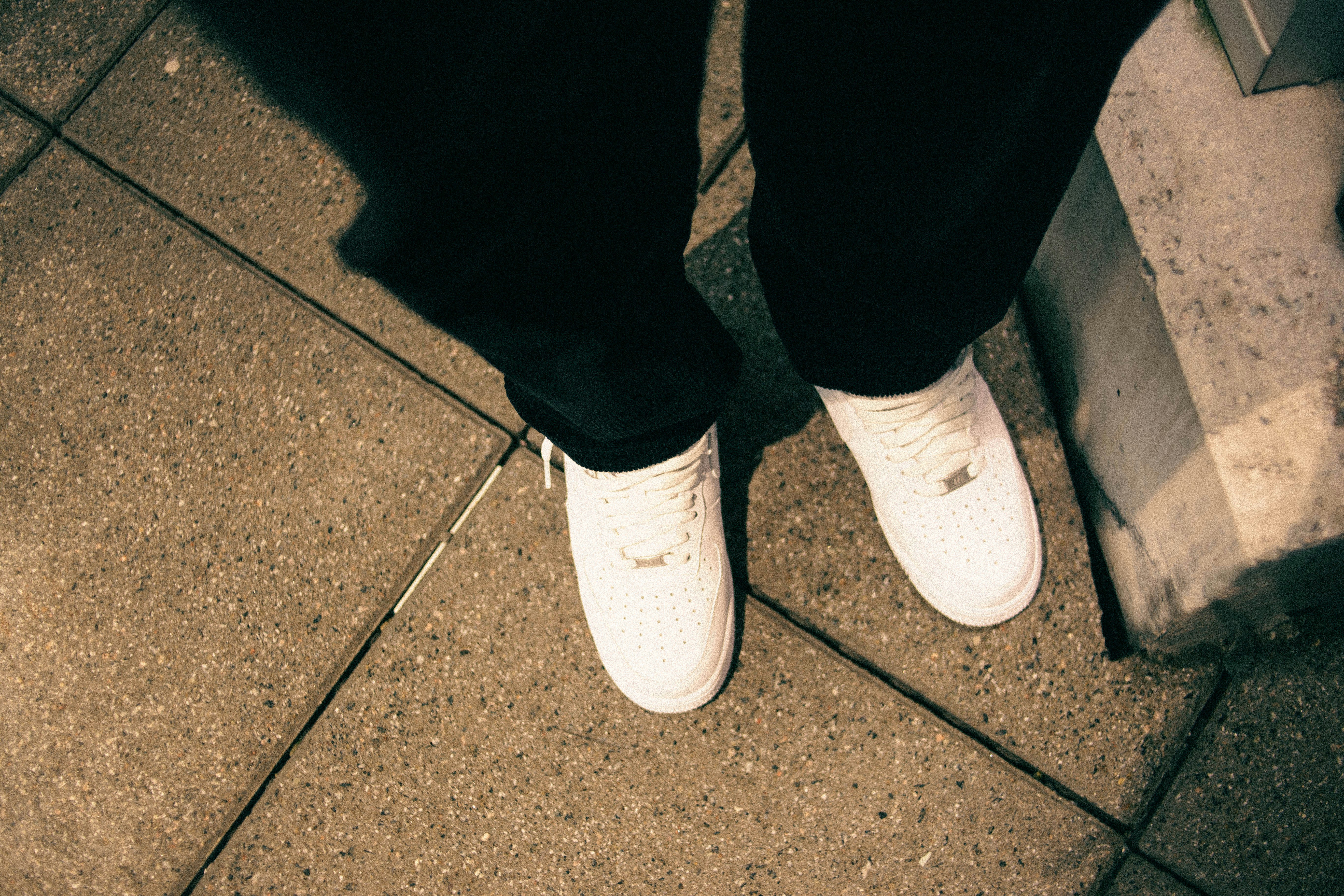 a person standing on a sidewalk with white shoes