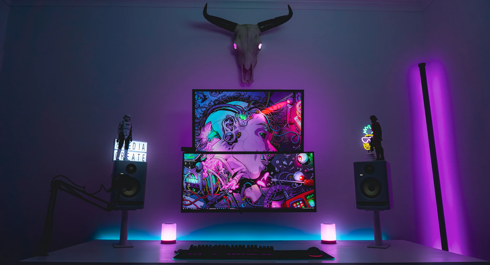 Dark gaming desk setup with monitor, desktop speakers and illuminated gaming equipment