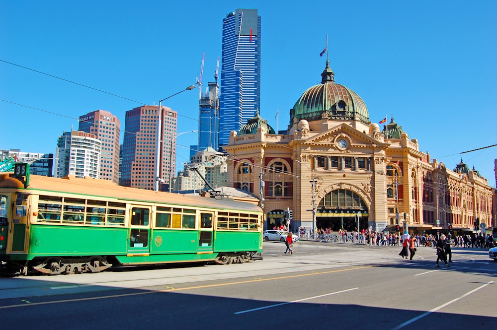 a green and yellow train traveling past a tall building