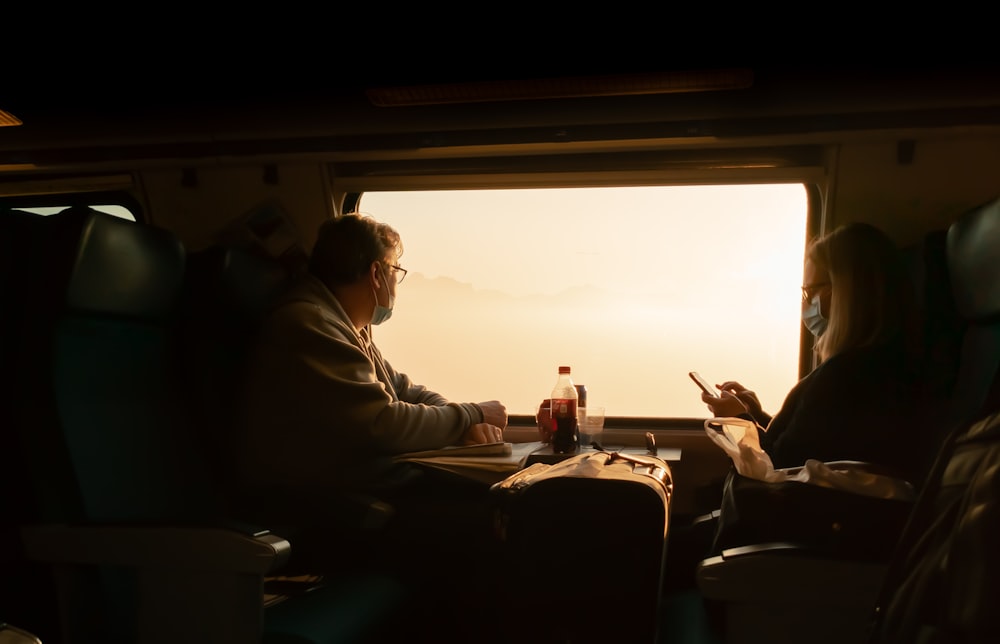 a man and a woman sitting on a train looking at their cell phones