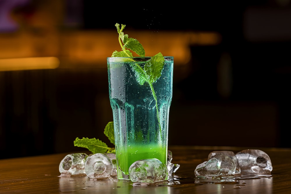 a green drink with ice cubes on a table