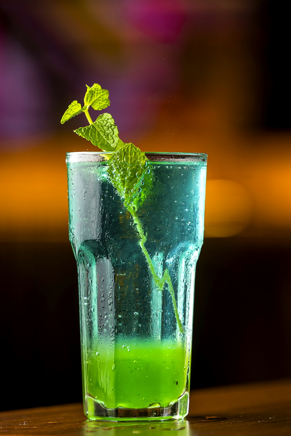 a glass filled with green liquid on top of a wooden table