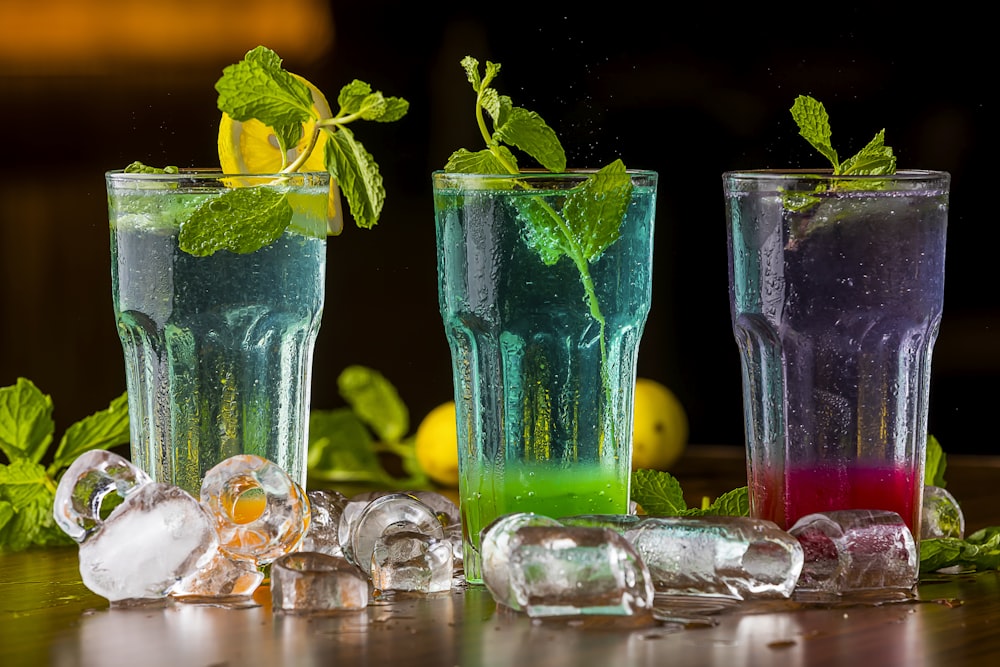 three glasses filled with different colored drinks