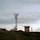 A telecommunications tower stands on a grassy hilltop, surrounded by a few small buildings. The sky is overcast with a layer of clouds, creating a calm and serene atmosphere.