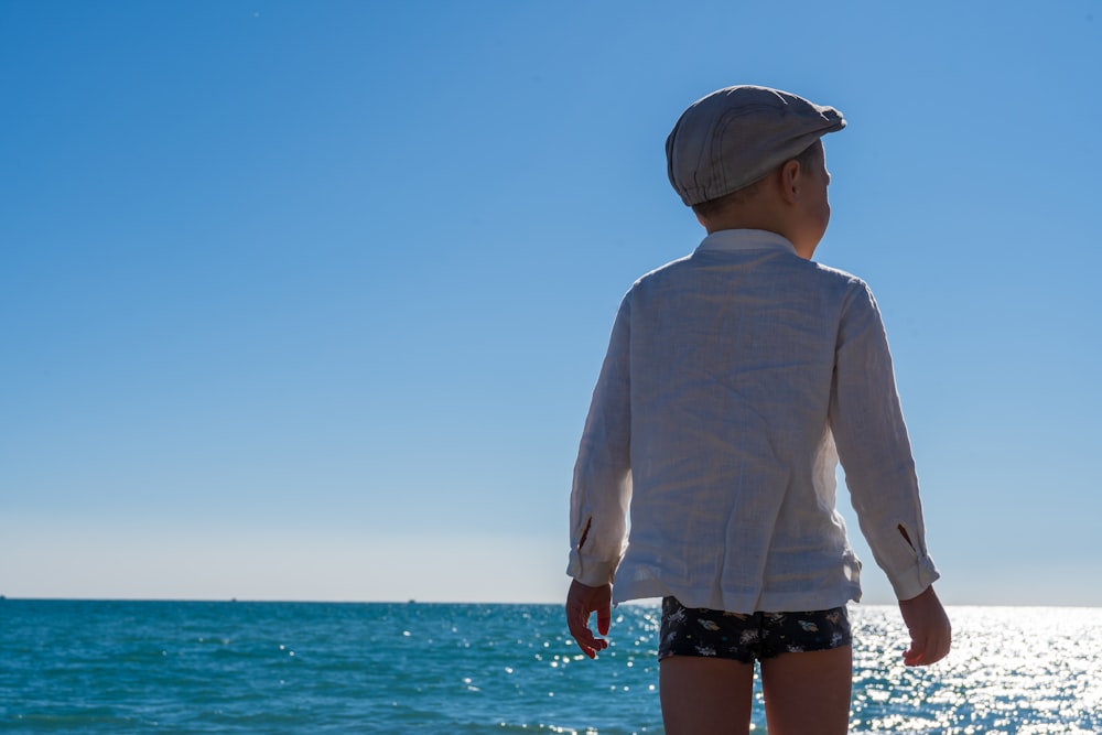 a little boy standing on a beach looking out at the ocean
