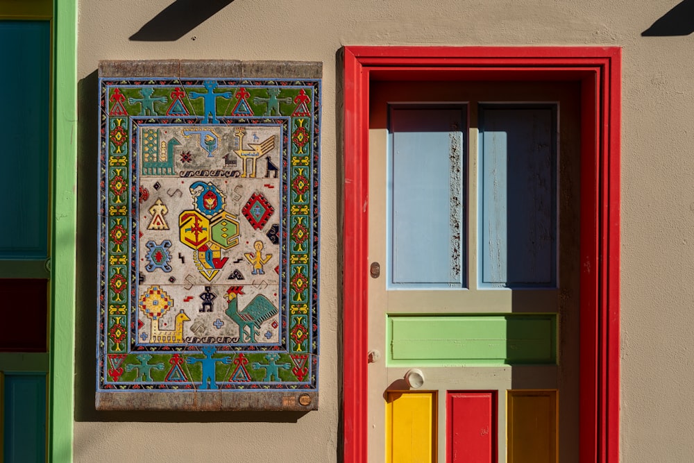 a multicolored wall hanging next to a red door
