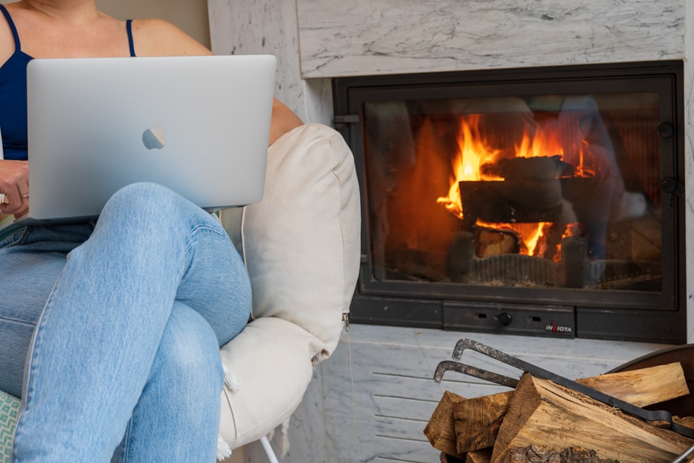 a woman sitting in a chair with a laptop in front of a fireplace