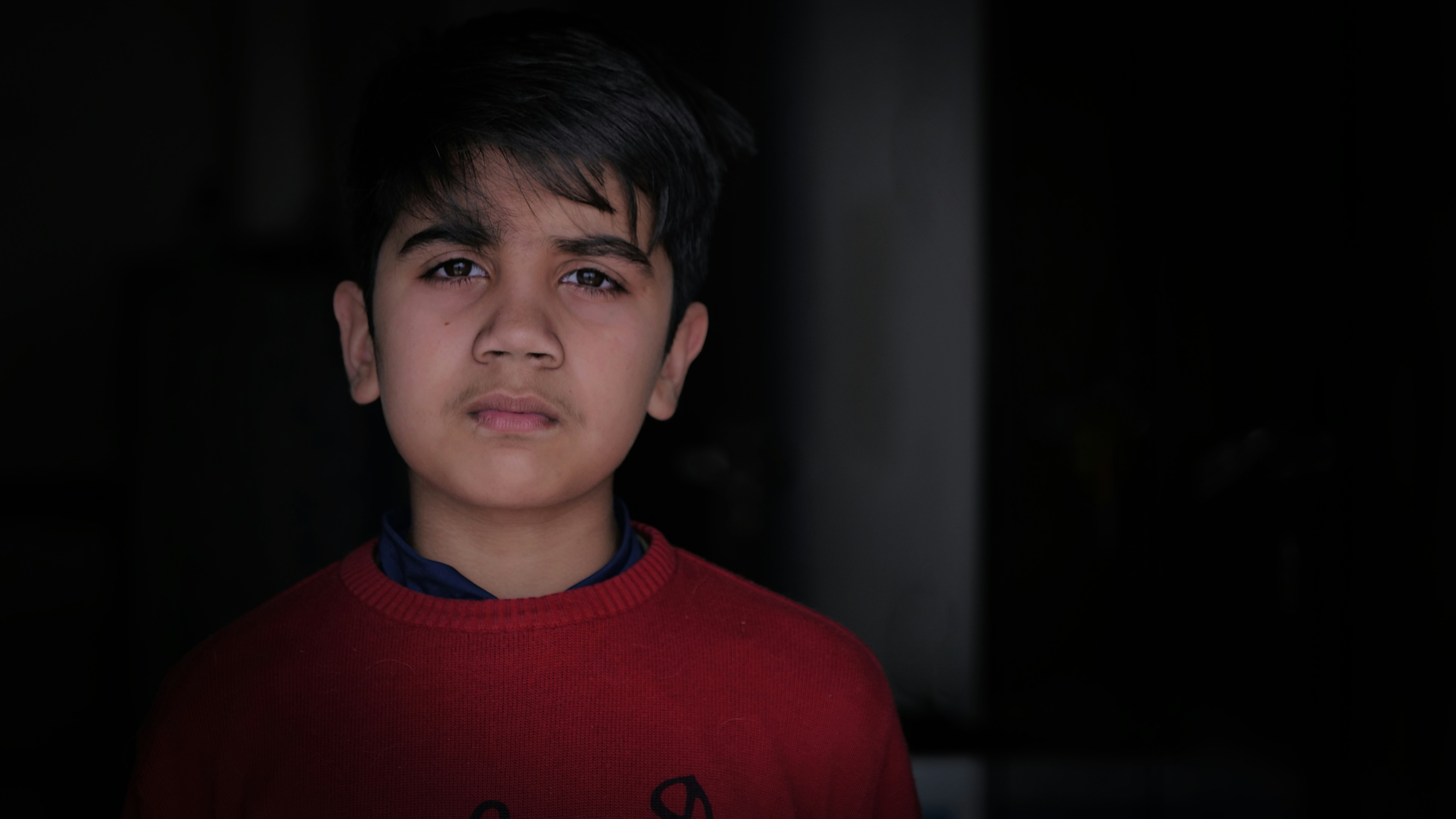 a young boy wearing a red shirt in a dark room