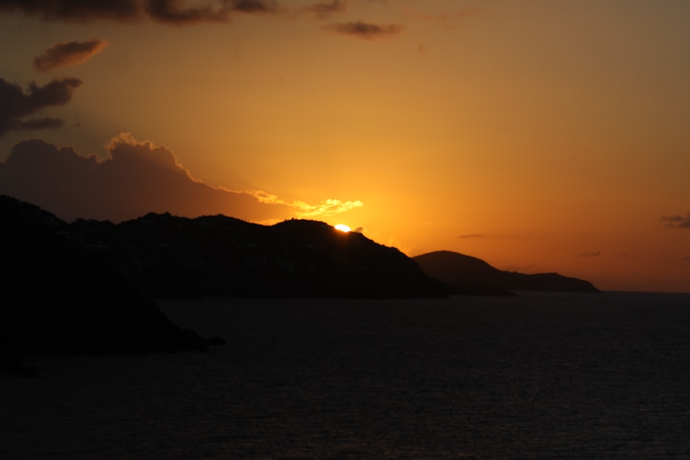 the sun is setting over the ocean with mountains in the background