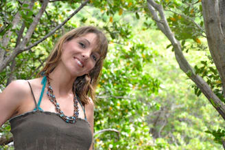 A joyful woman wearing layered minimalist necklaces and bracelets, smiling outdoors.