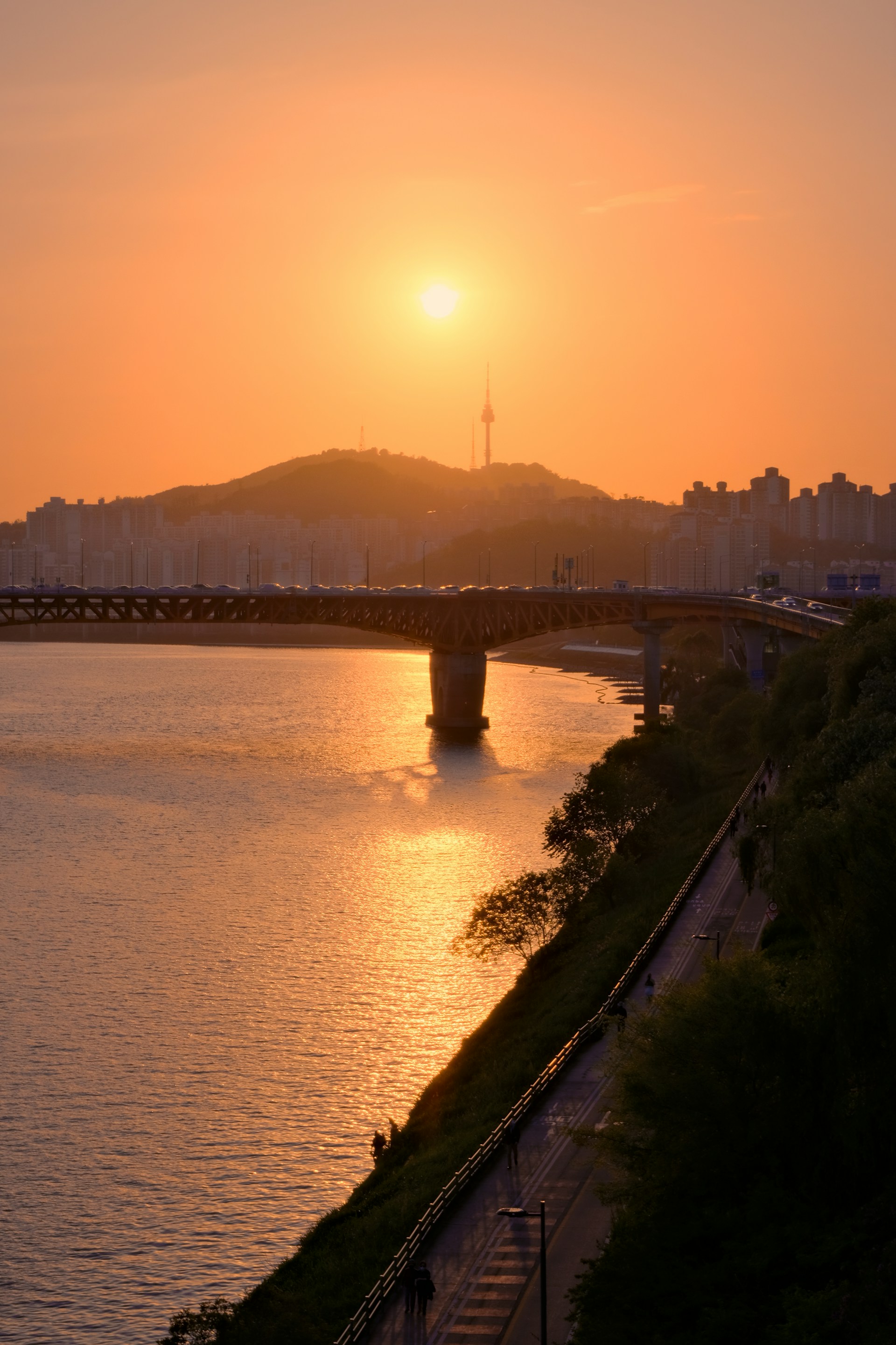 the sun is setting over the water and a bridge