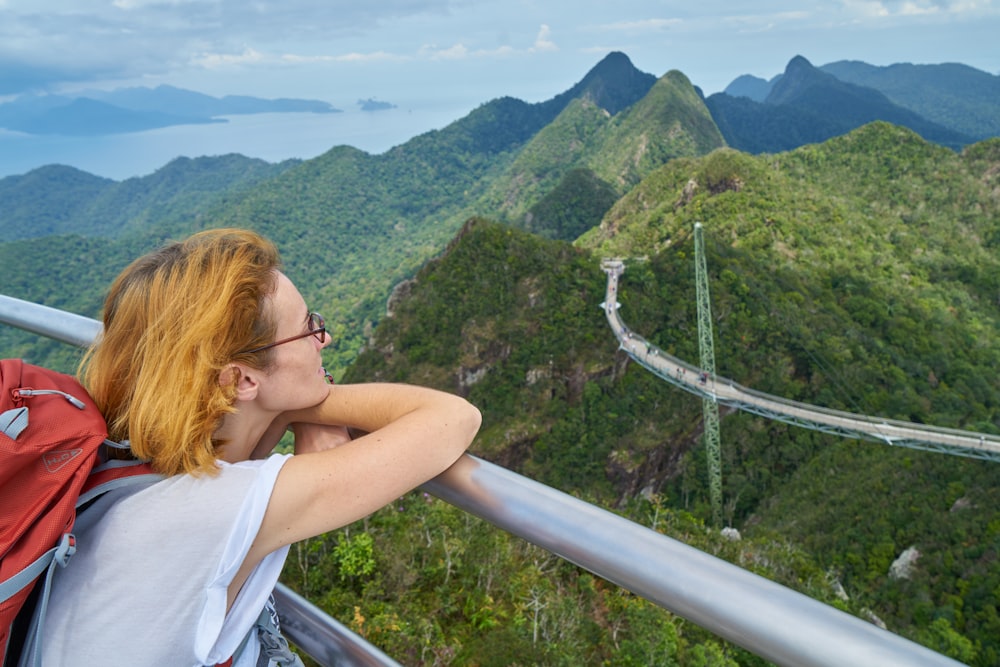 a woman with red hair and glasses standing on a bridge