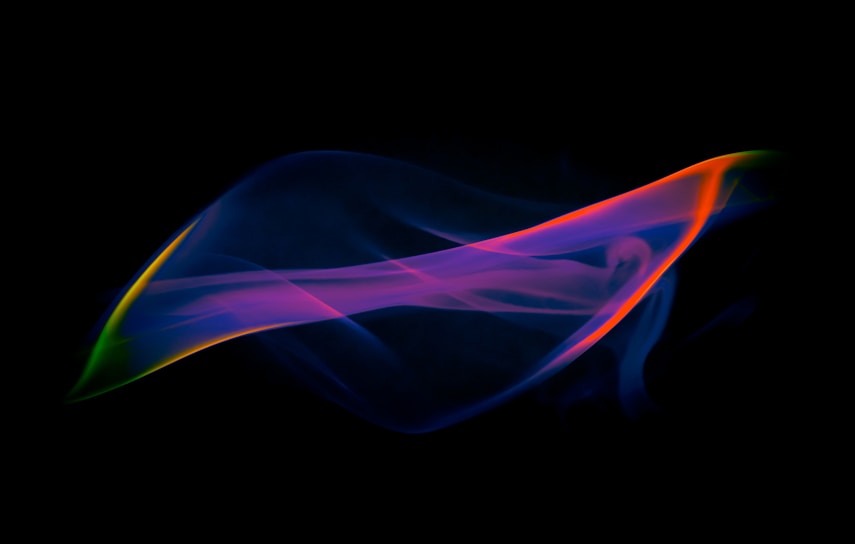 A swirl of colorful incense smoke rising against a deep black background, with hints of bright blues and warm oranges.