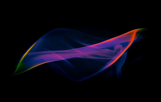 A swirl of vibrant, multicolored smoke against a black background, featuring hues of purple, blue, orange, and green blending seamlessly in a fluid, abstract form.