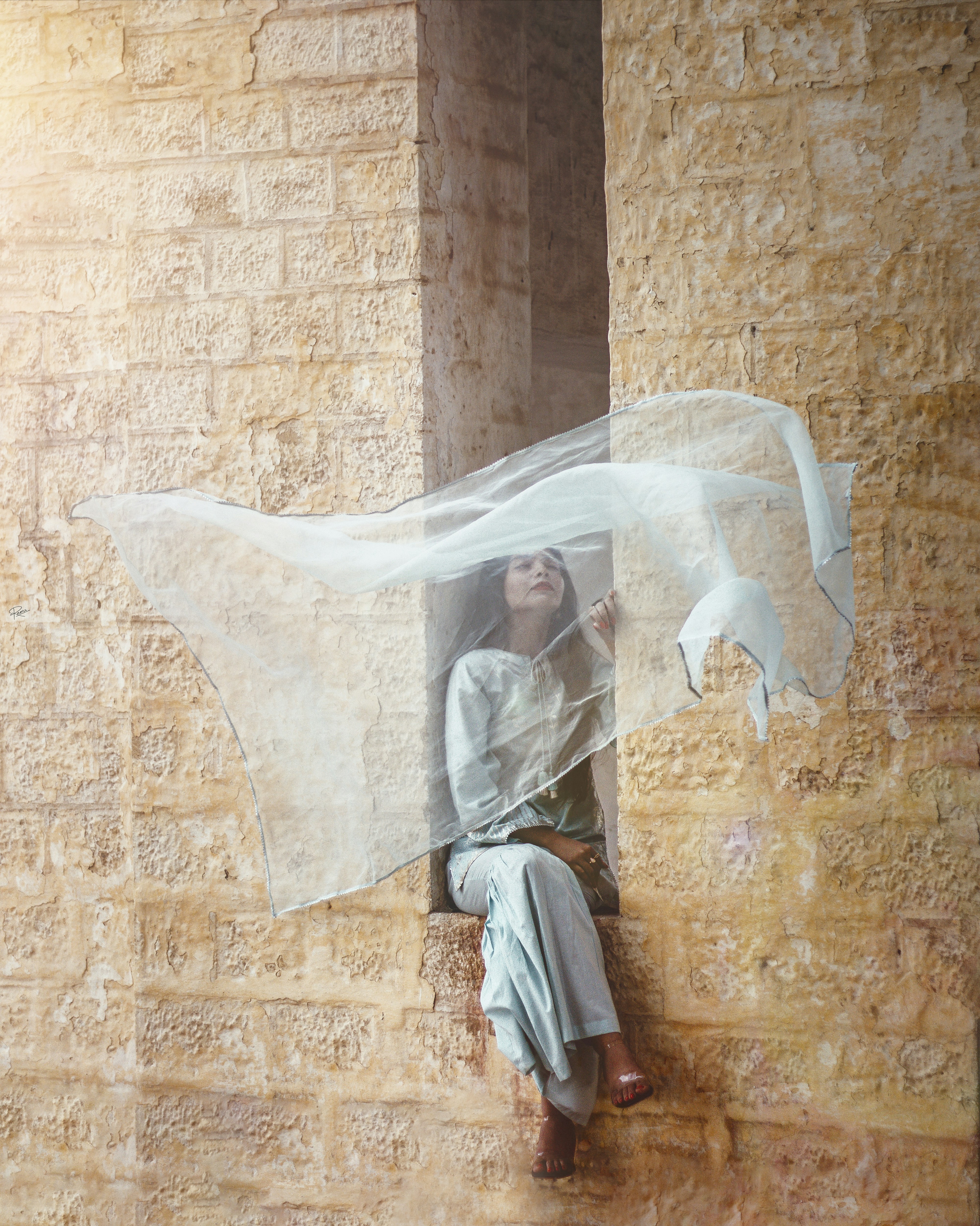 a woman sitting on a ledge with a veil over her head