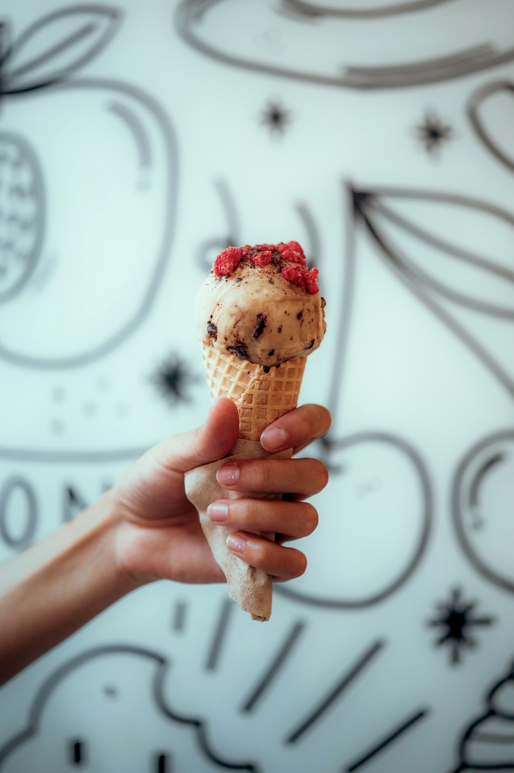 a hand holding an ice cream cone with berries on top