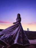 Model wearing a flowing mystical robe with celestial prints under a sunset sky.