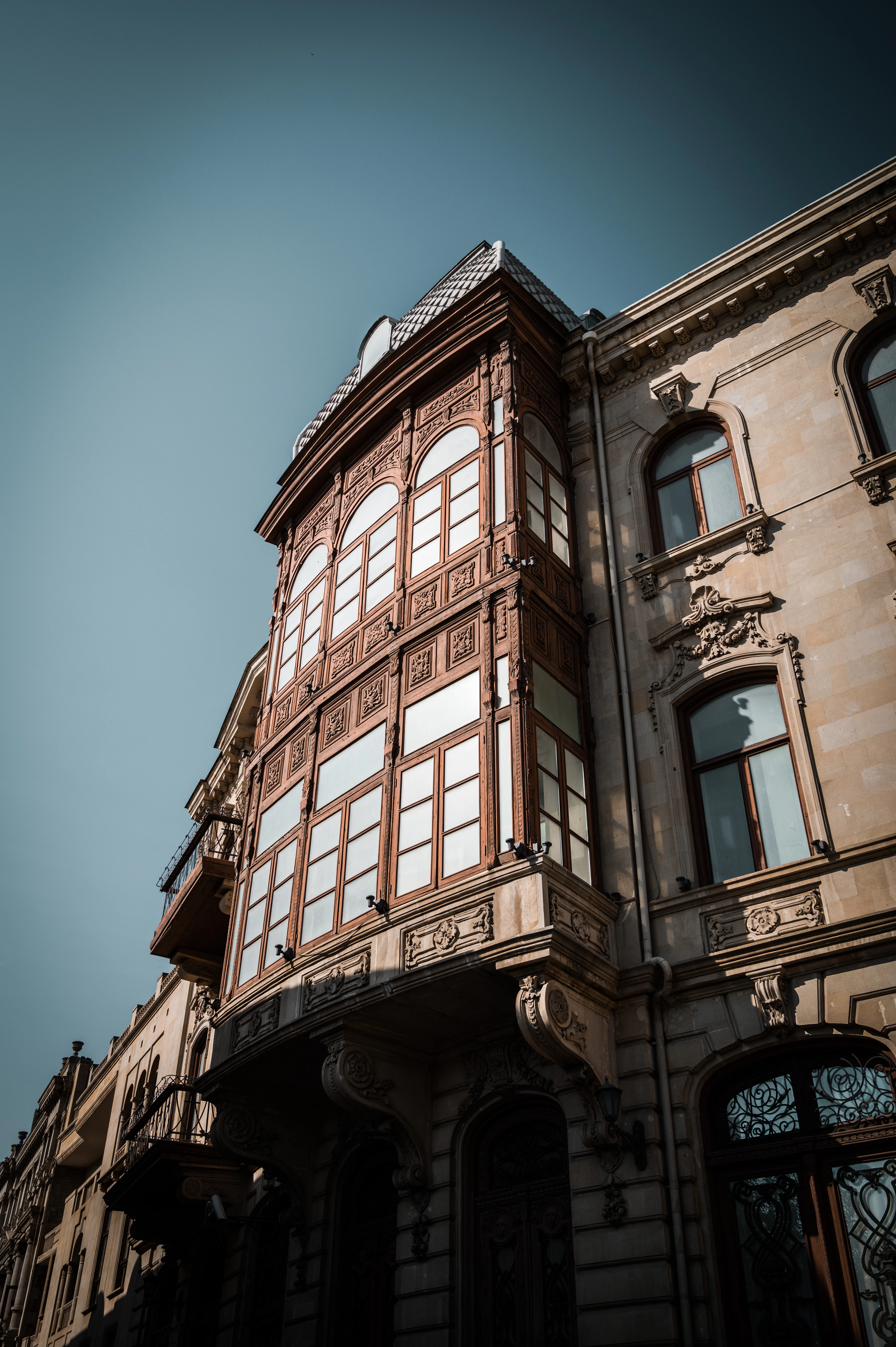 A bay-windowed corner building glows warmly against a dramatic dark teal evening sky in Baku.
