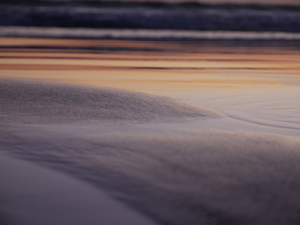 a close up of sand and water with a sunset in the background